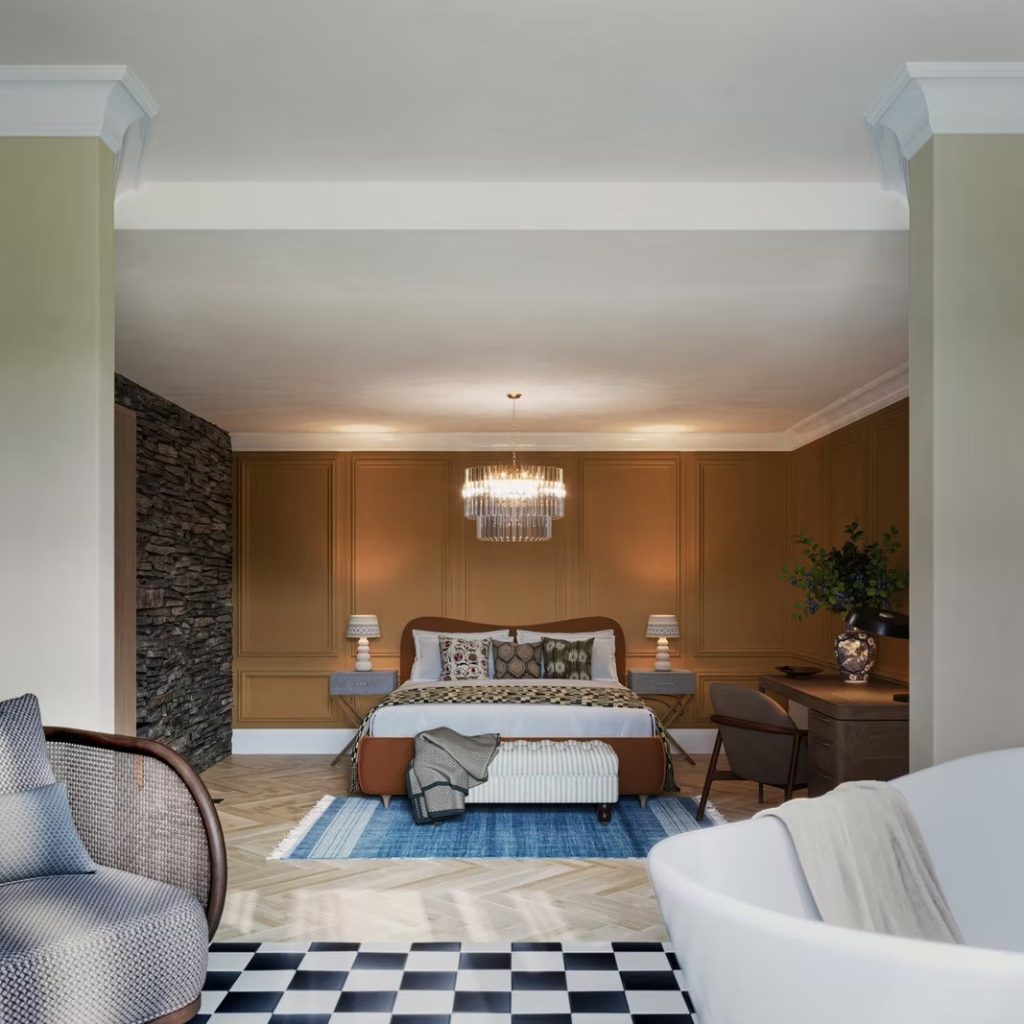 Expansive suite with panelled walls, a stone-clad recess and a freestanding bath, anchored by a glass chandelier.