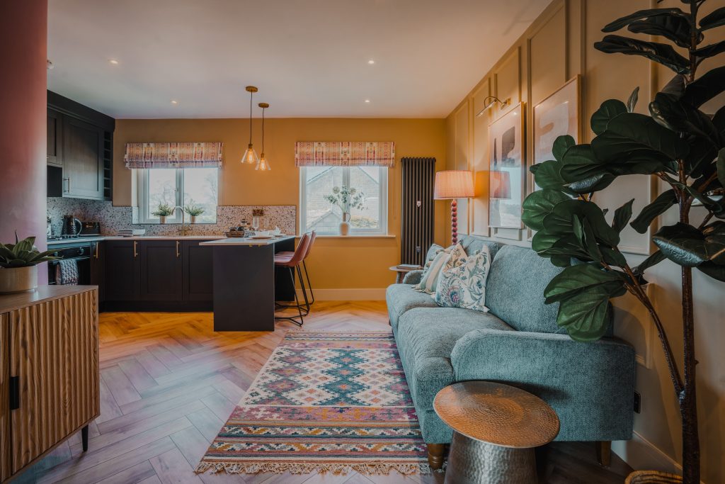 Discover a beautifully designed serviced accommodation in Beckwithshaw, North Yorkshire featuring an open-plan living area with mustard-yellow paneled walls, a sleek black kitchen island...