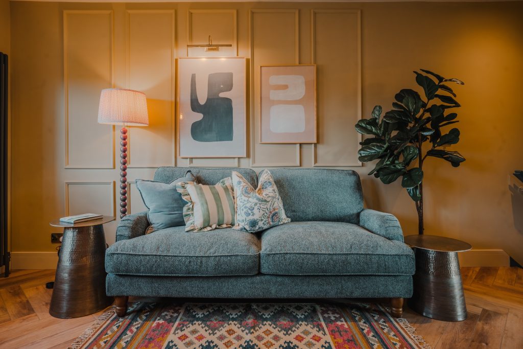 Discover this stylish living area in Beckwithshaw, North Yorkshire serviced accommodation. Featuring a plush teal two-seater sofa with patterned cushions, wall-mounted abstract artwork...