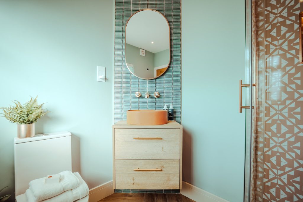 Discover a stylish ensuite in our Beckwithshaw, North Yorkshire serviced accommodation. Featuring a terracotta vessel sink atop a floating oak vanity, brass wall-mounted faucet set against...
