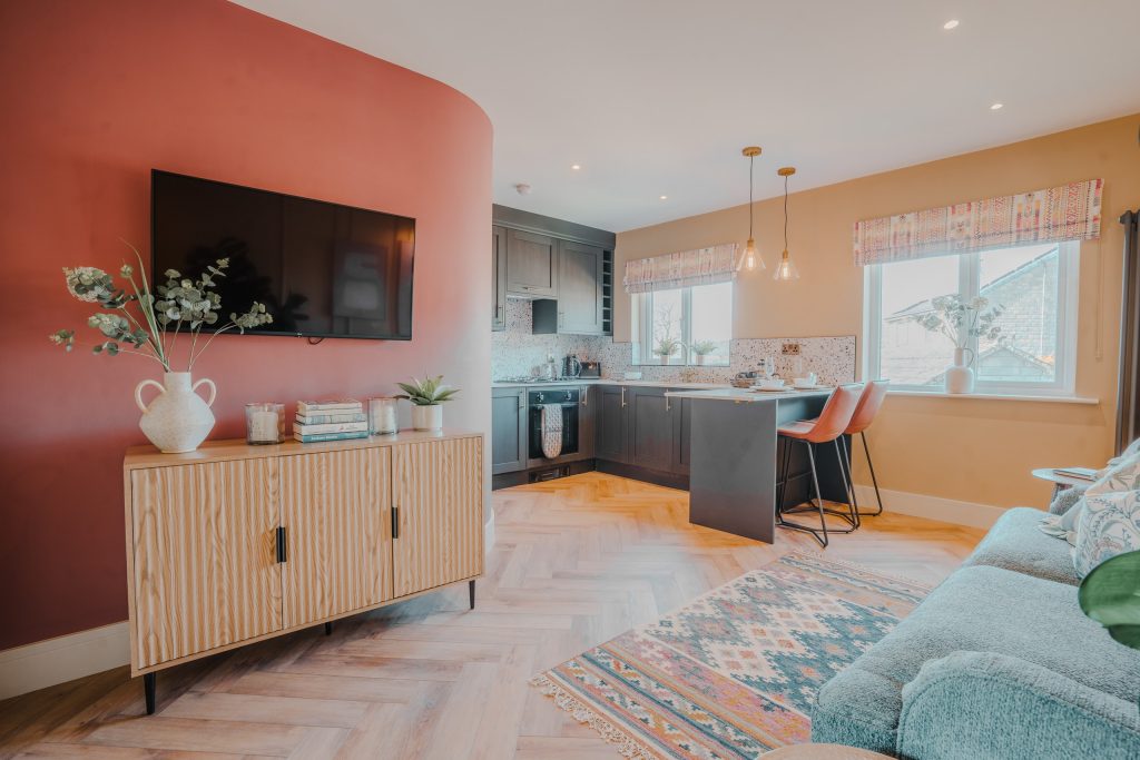 Experience stylish countryside living in Beckwithshaw, North Yorkshire. This serviced accommodation features a curved red accent wall with mounted TV, wood-grain sideboard, sleek black...