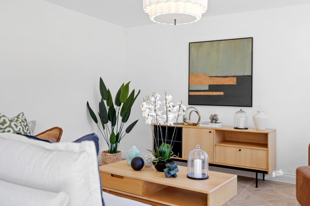 Living room staged with a soft neutral sofa, a light wood sideboard styled with orchids and sculptural decor, and abstract wall art.
