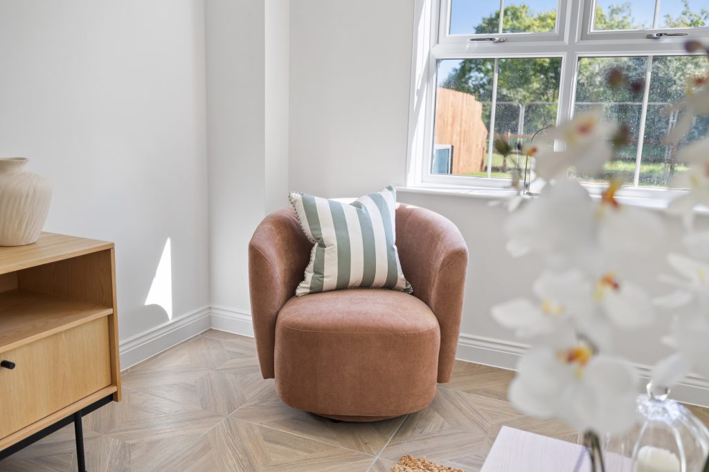 Bedroom corner with a rust swivel armchair, a light wood dresser and a bright window framed by spring blossom.