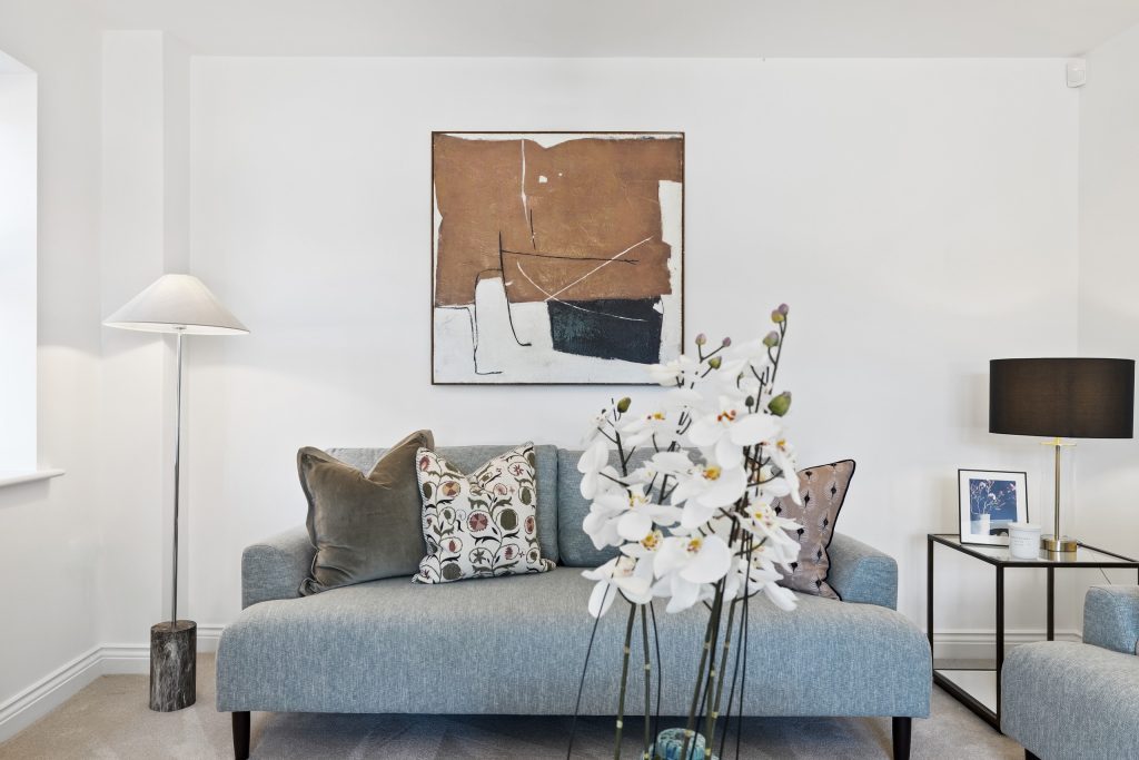 Living room with a soft blue sofa layered with patterned cushions, a floor lamp and a warm abstract artwork.