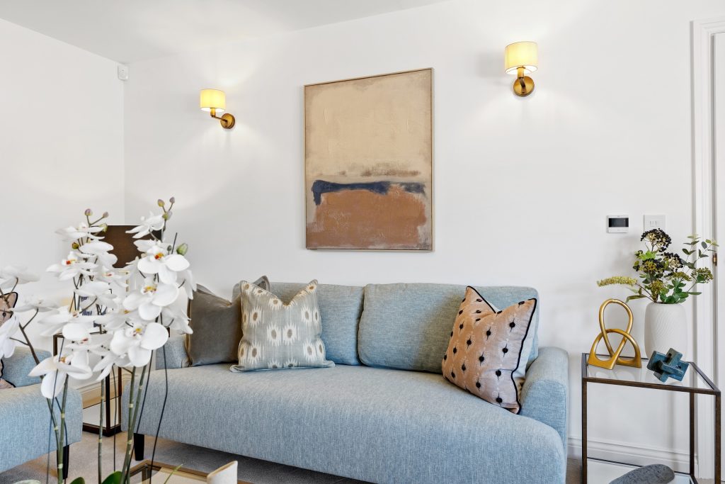 Living room with a blue sofa, brass wall lights, a gold-accented side table and a calm abstract print.