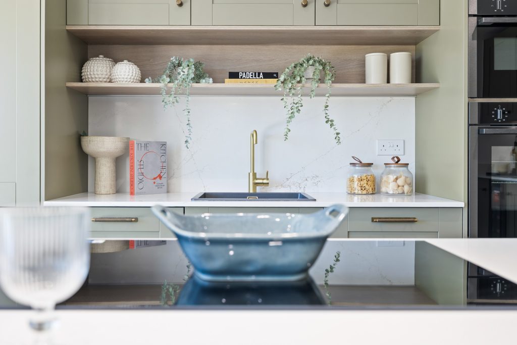 Kitchen with sage and cream cabinetry, a brushed-gold tap, open shelving and softly styled worktops.
