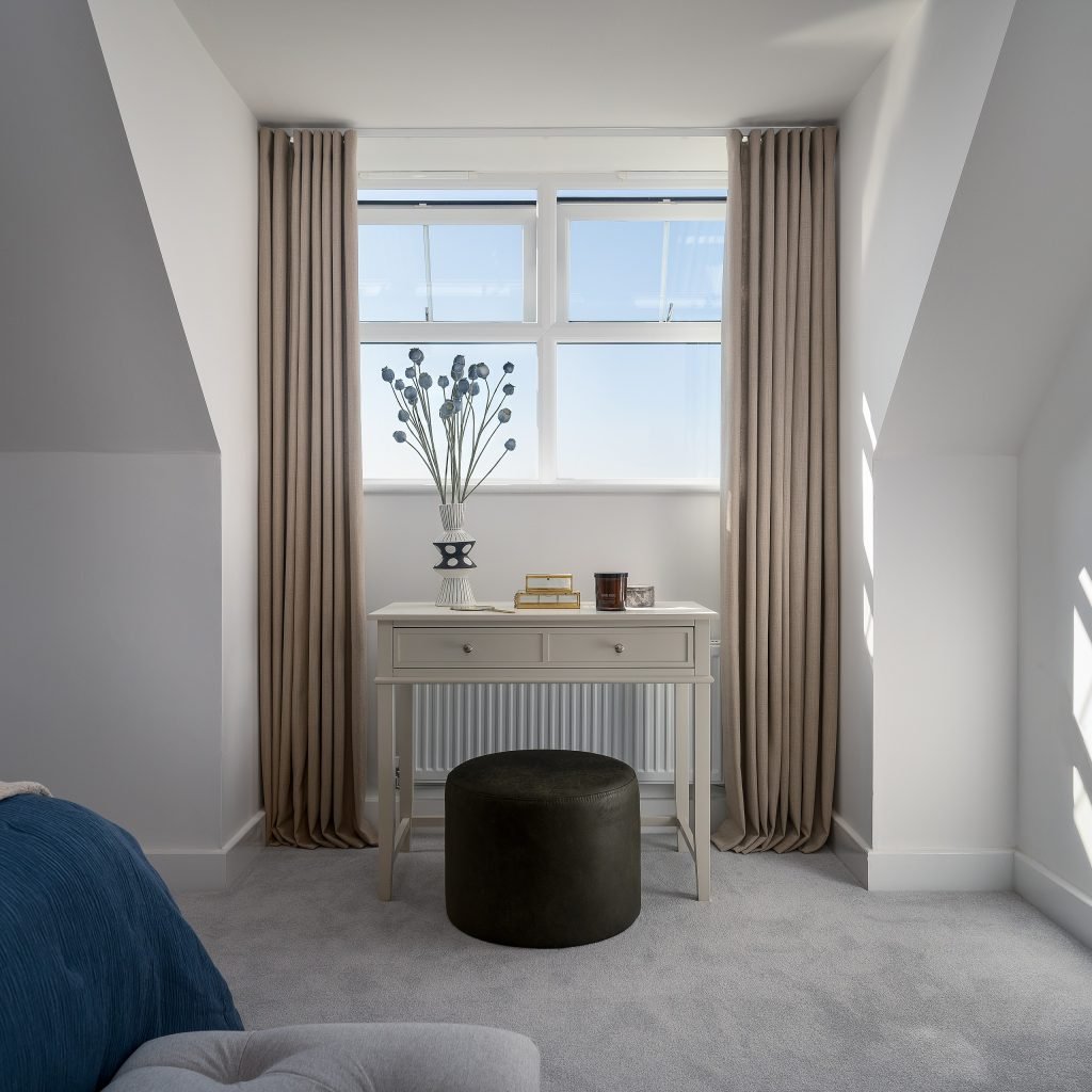 Discover the Foxes Chase home’s serene dressing nook in East Riding Yorkshire, featuring a fitted console table beneath a bright window, plush stool, and soft neutral drapes