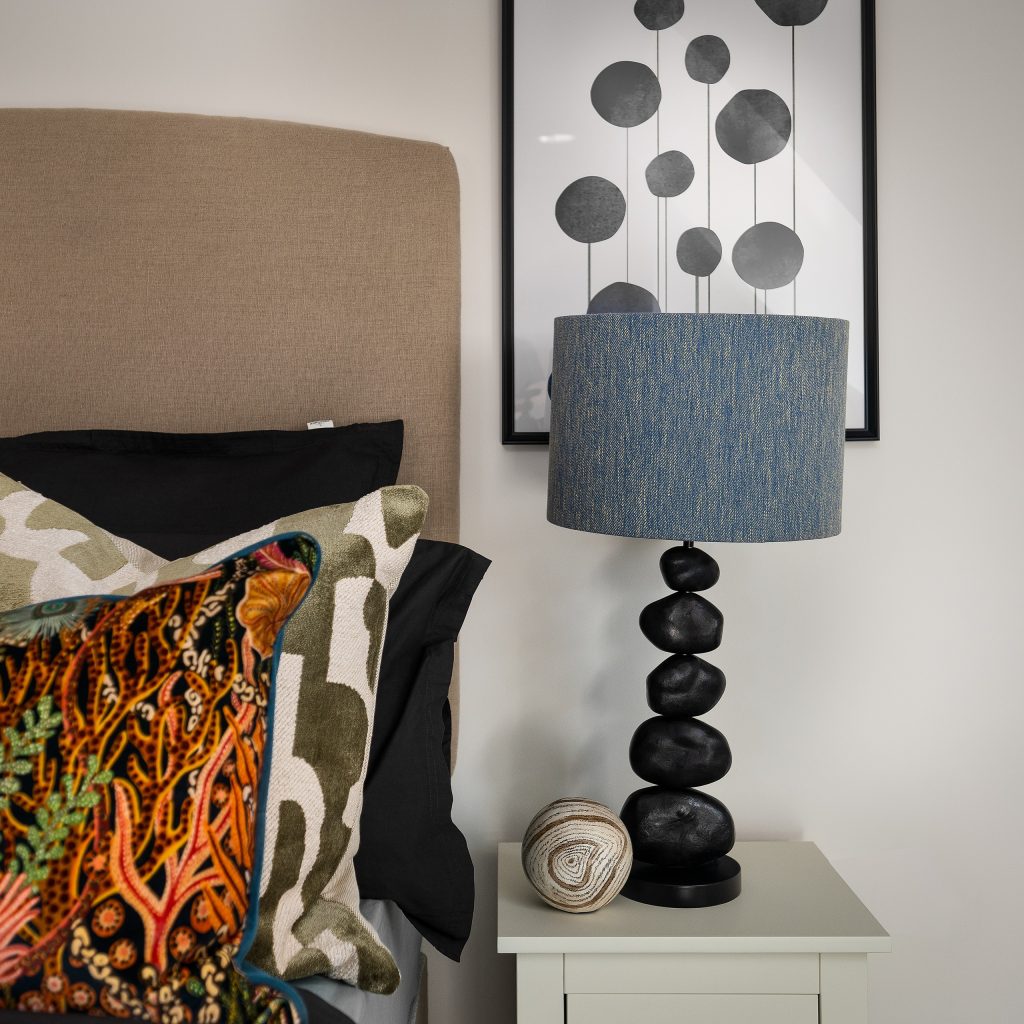 Explore the Foxes Chase home’s chic bedside styling in East Riding Yorkshire, featuring a stacked-stone lamp with a blue shade, patterned pillows, and modern wall art.