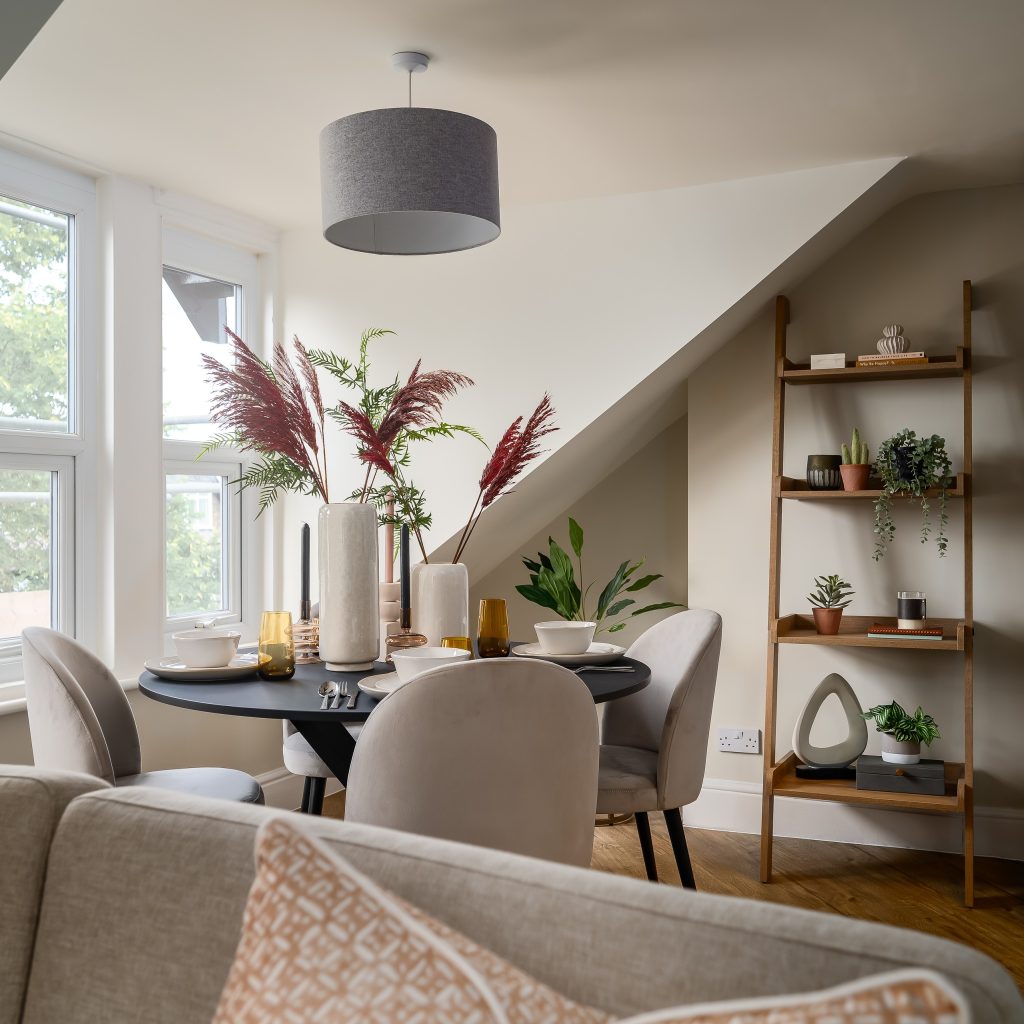 A beautifully staged dining nook in a Grove Road, Harrogate property by WildKind Interiors. This setup features a matte black round table set for four with neutral dinnerware, amber-hued...