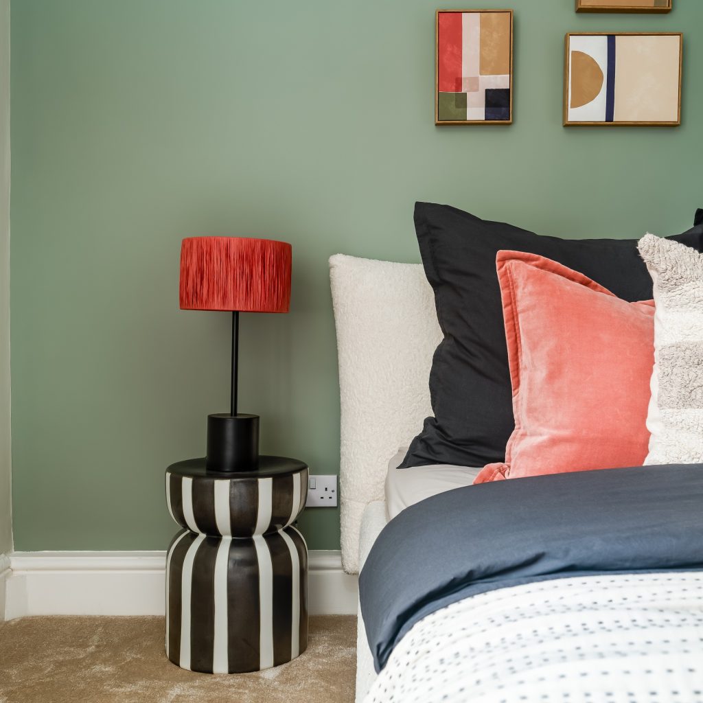 A striking bedroom accent vignette staged by WildKind Interiors for a Grove Road, Harrogate property. Featuring a sage-green accent wall behind a plush bed layered with black, coral velvet...
