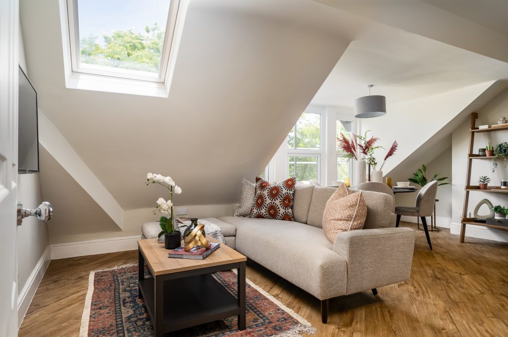 Living space set under the eaves with a soft neutral sofa and warm accent lighting.