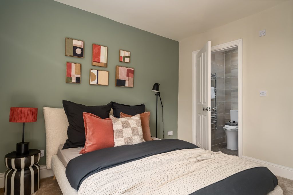 Bedroom with a sage-green feature wall, coral and black accent cushions and abstract art.