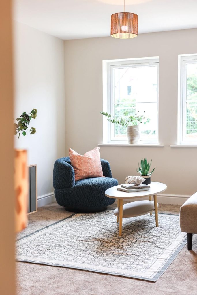 A warm seating corner in a Huntingdon, York home professionally staged by WildKind Interiors. The vignette features a textured navy armchair accented with a blush pink cushion, a light wood...