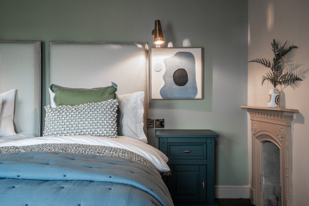 A tranquil bedroom detail in Magazine Lane serviced accommodation, The Wirral, styled by WildKind Interiors. This vignette features twin striped upholstered headboards with coordinating...