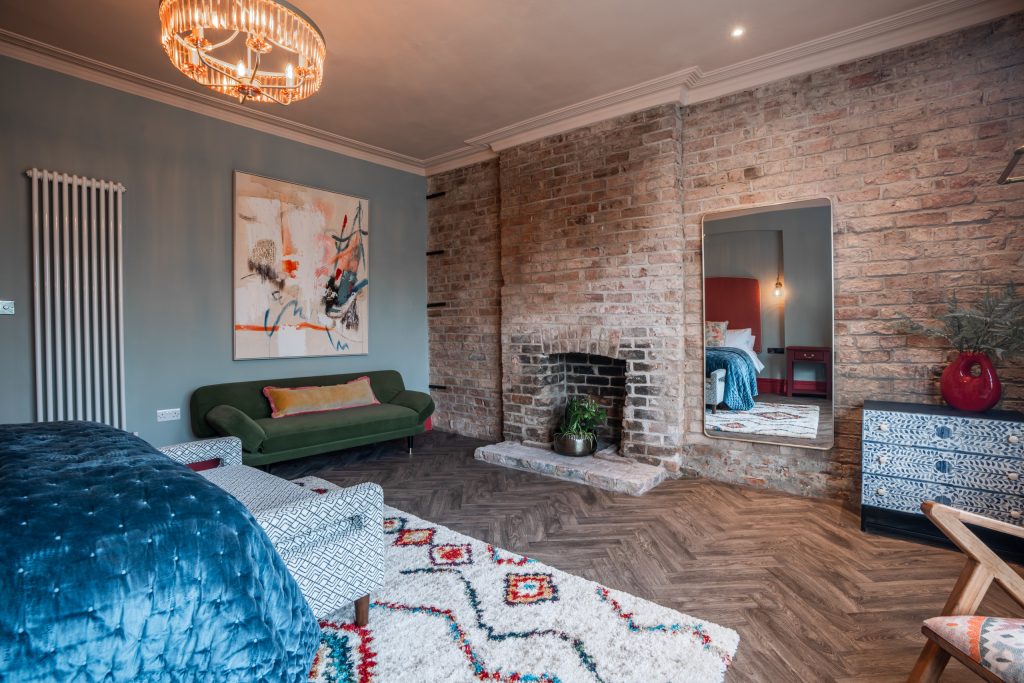 Living room with an exposed brick fireplace, an emerald green sofa and a characterful bay window.