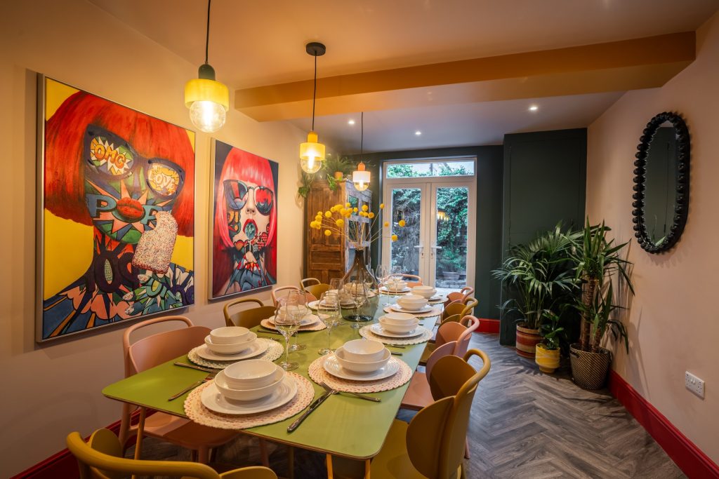 Dining room with a pastel-green table, mismatched colourful chairs and bold pop-art on the walls.