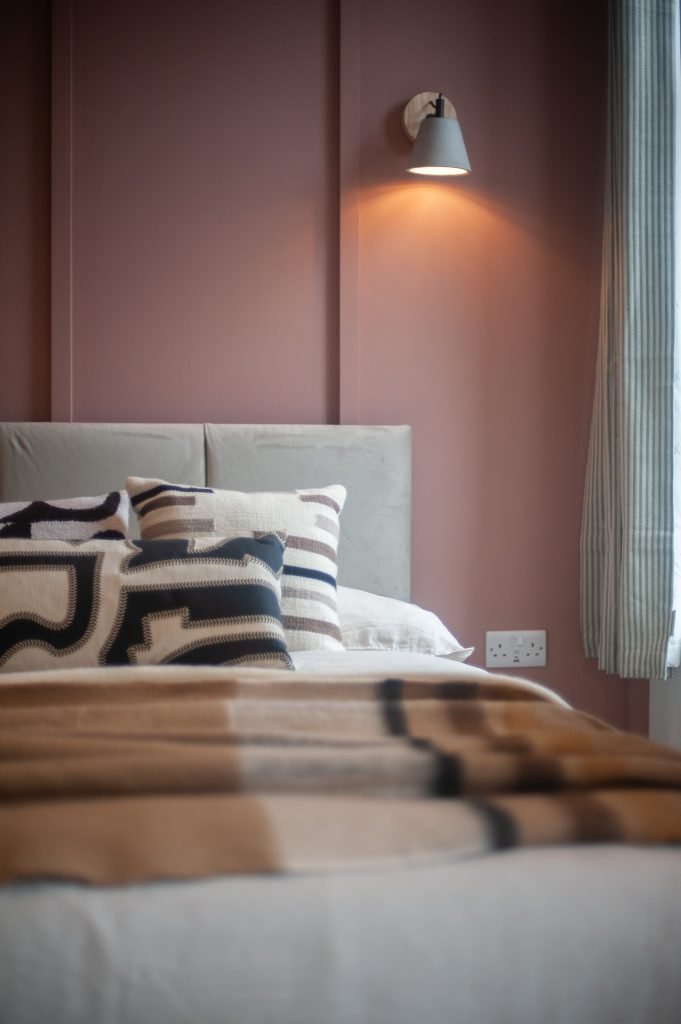 Tenant bedroom with a soft pink feature wall, cream headboard and layered textured bedding.