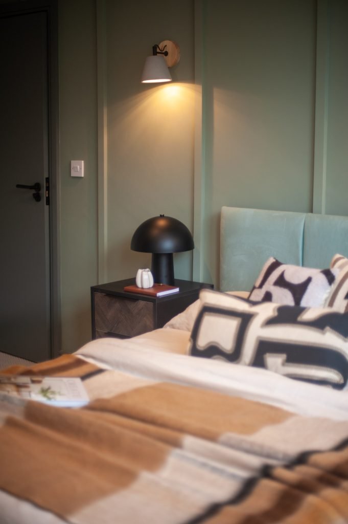 Tenant bedroom with a sage-green panelled wall, teal headboard and a timber bedside table.
