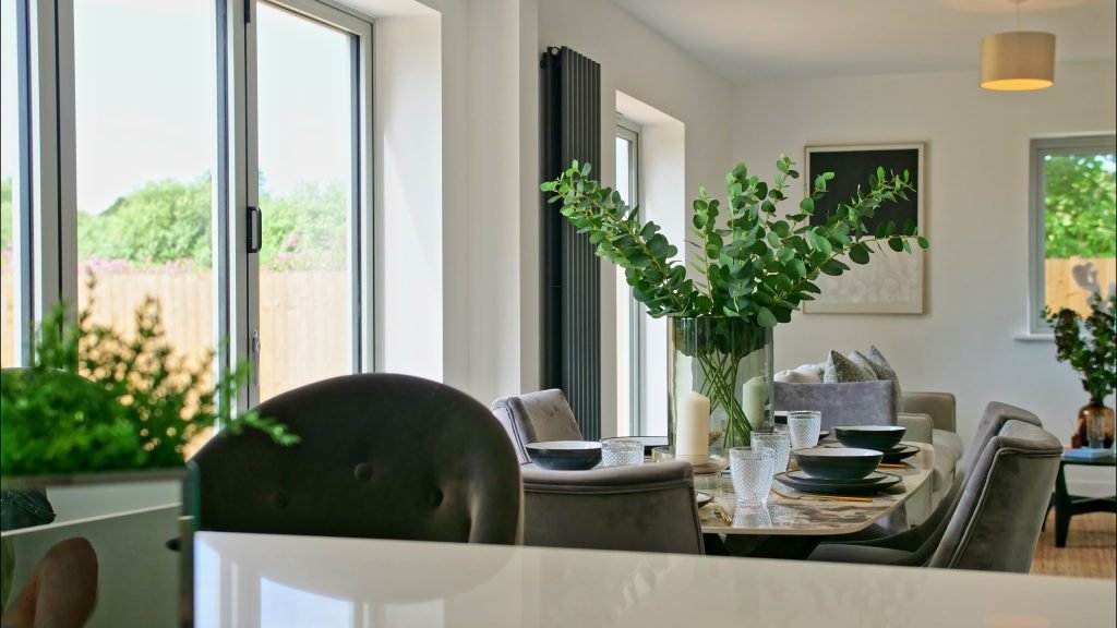 Open-plan dining area viewed across the kitchen island, with a round table, velvet chairs and a tall eucalyptus arrangement beside the garden doors.