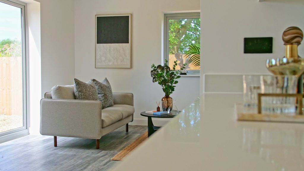This high-resolution image showcases a stylish, staged-for-sale open-plan living space in Greater Manchester. A light grey two-seater upholstered sofa, dressed with charcoal-textured...