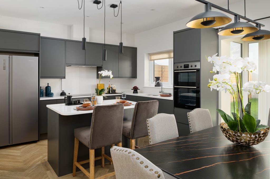 A contemporary open-plan kitchen and dining area professionally staged by WildKind Interiors. This project features sleek dark cabinetry, a white island with barstool seating, modern...