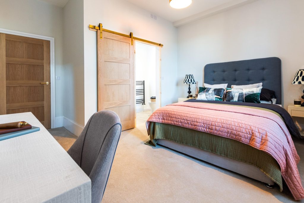 This expertly staged master bedroom in Scartho, Lincolnshire features a contemporary grey upholstered headboard bed dressed in layered bedding: an olive-green quilt topped with a dusty-rose...