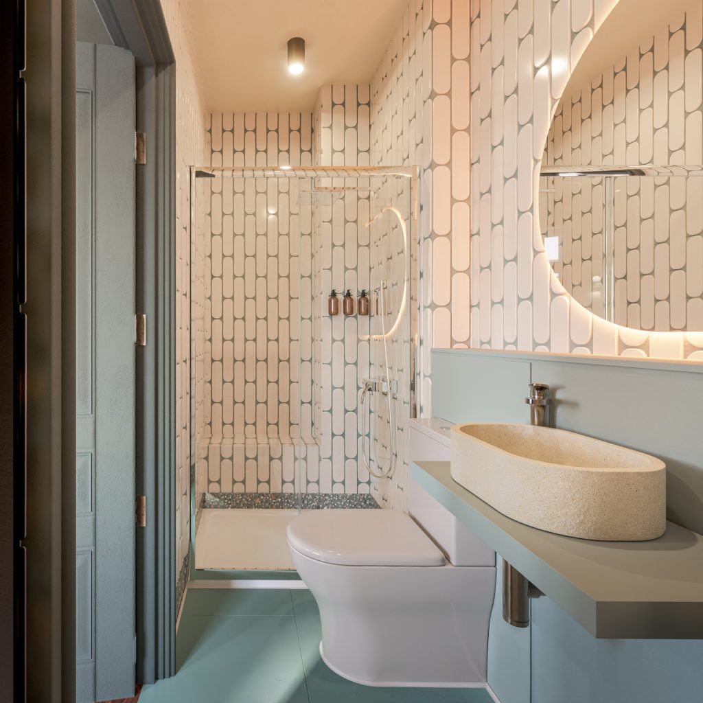 Shower room with patterned tiling, a sage vanity, a round mirror and a walk-in shower.