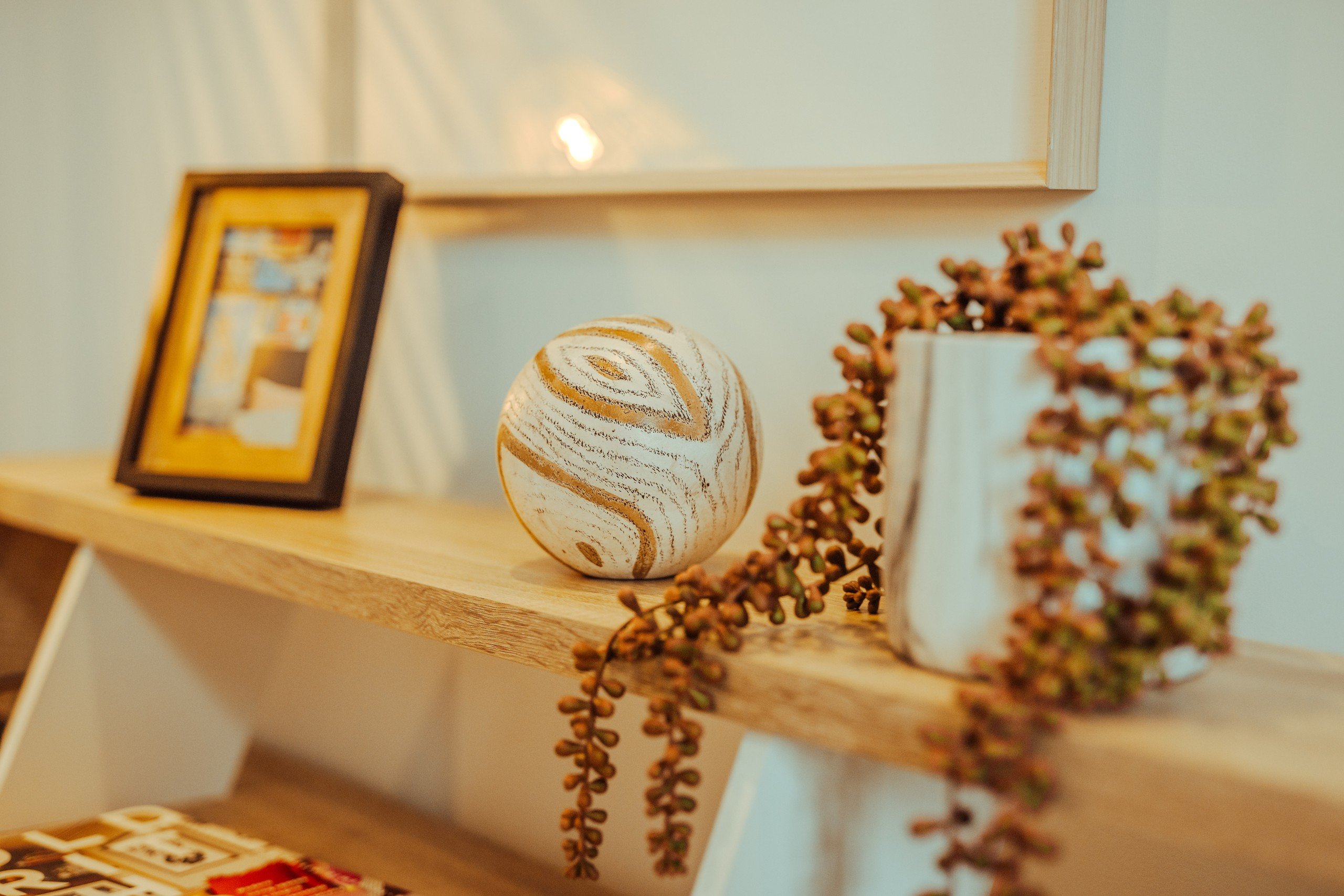 Wooden shelf with a patterned sphere, framed photo, and potted plant against a light wall. Soft lighting creates a cozy ambiance.