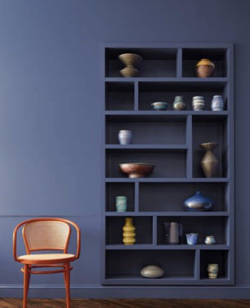 A blue painted wall in the background with a bright orange chair in the foreground