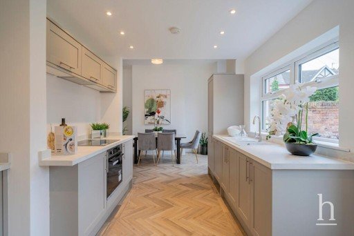 Modern kitchen with light gray cabinets, a chevron-patterned floor, and a dining table. Large windows and white orchids add brightness.