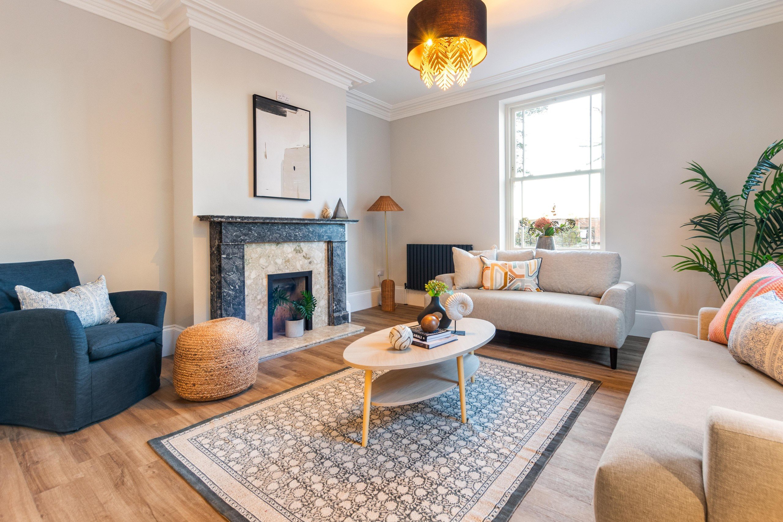 Cozy living room with beige sofas, blue patterned rug, and modern art. A bright lamp glows above a wooden coffee table with decor.